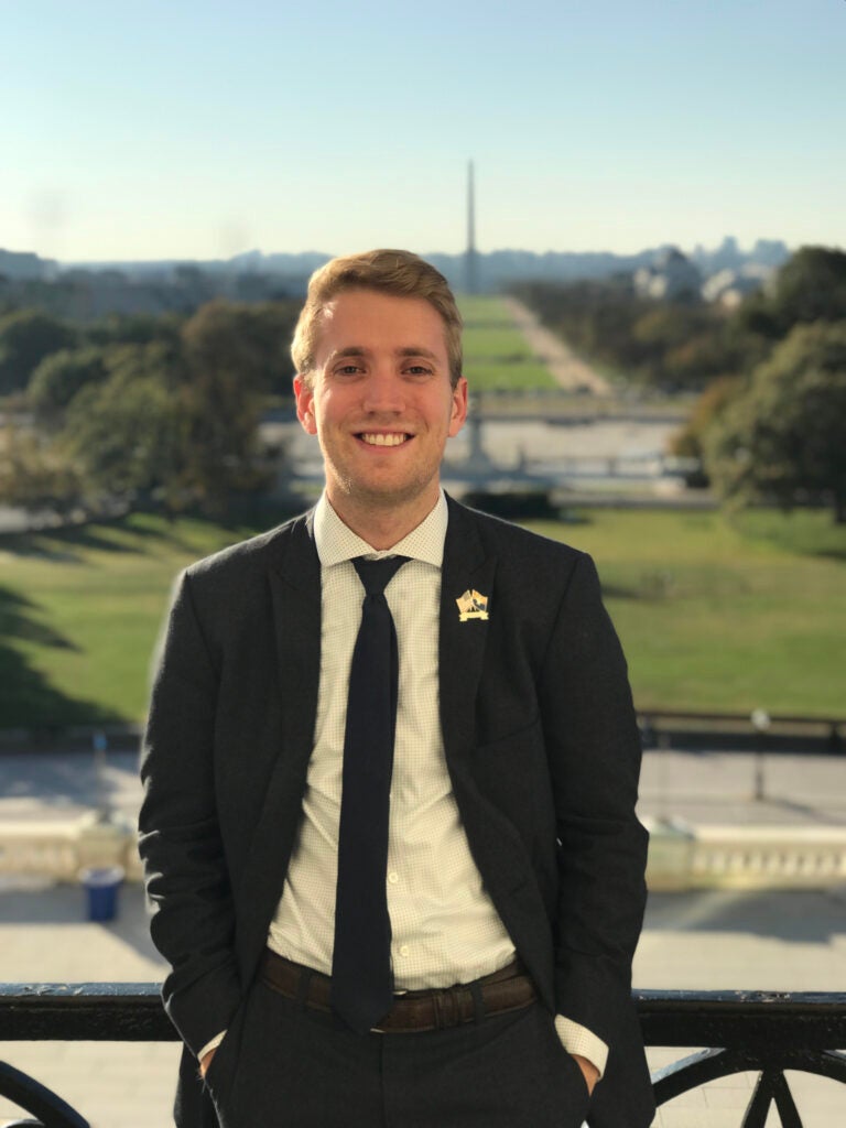 Dustin Vesey stands on the balcony of the United States Capitol, smiling at the camera.