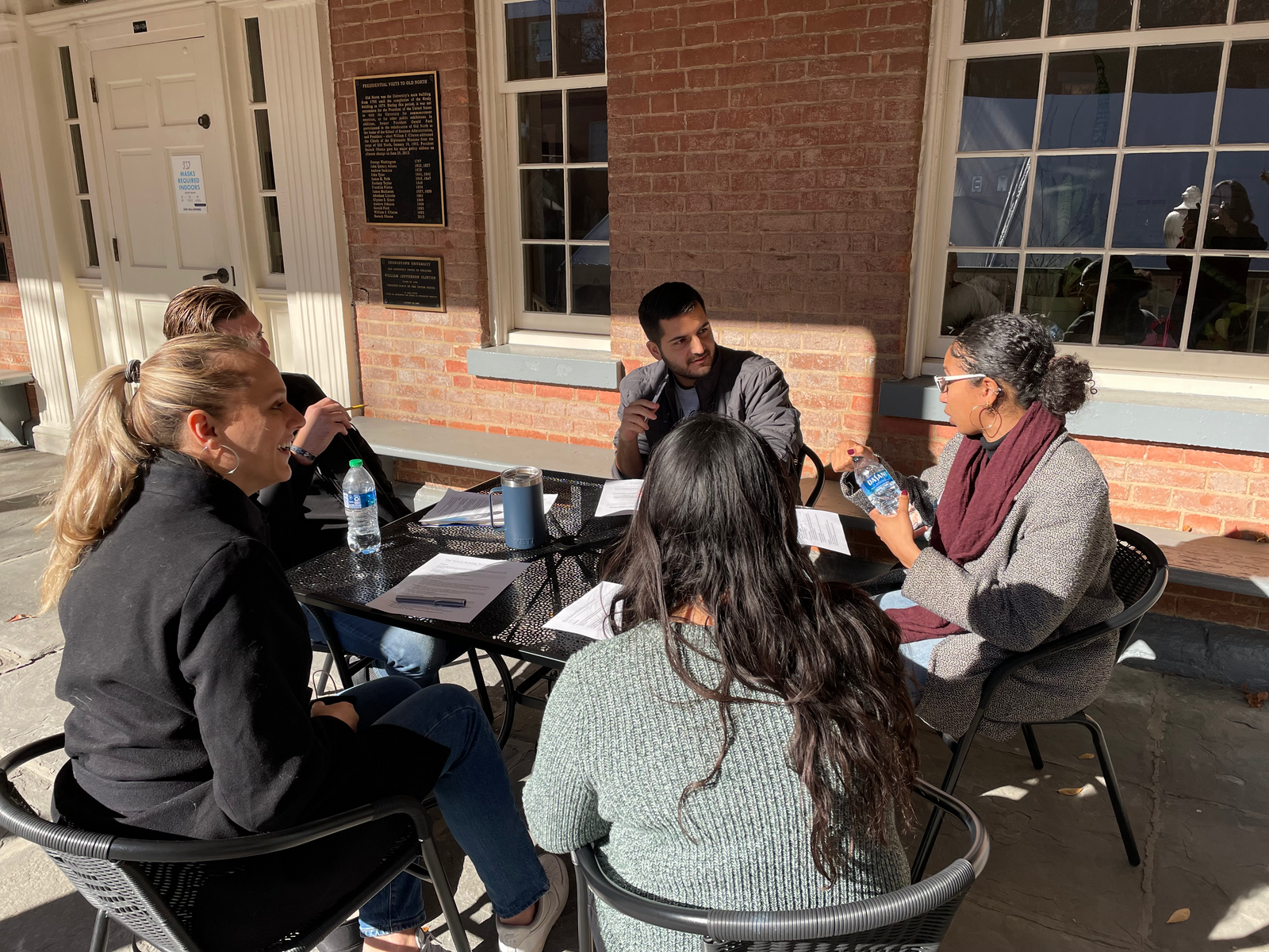 A group of students sits outside laughing as they discuss a case.